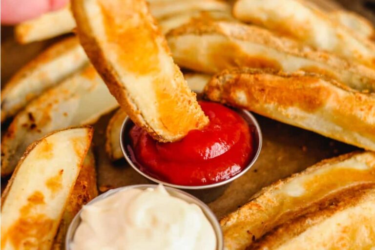 Potato wedges being dipped in sauce.