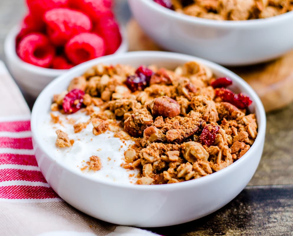 A bowl of protein granola with fresh raspberries in the background.
