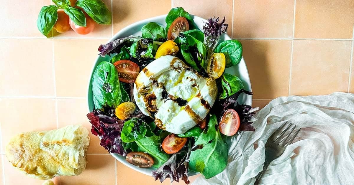 burrata salad with balsamic glaze including spring mix, basil leaves, halved cherry tomatoes, drizzled with balsamic glaze and olive oil.