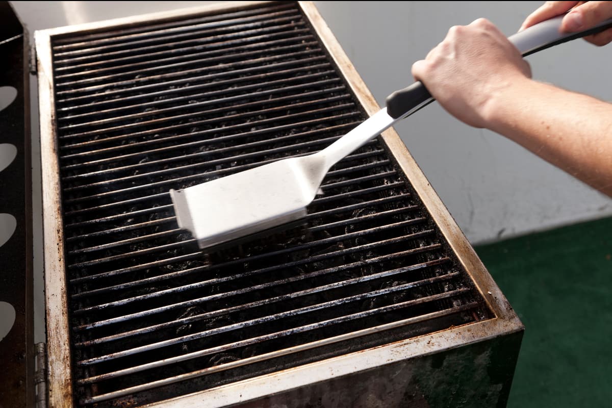 Grill being scraped with a brush.