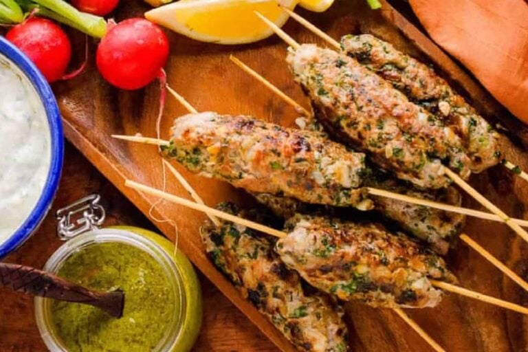 Lamb kofta kebabs on a wooden board with fresh herbs and vegetables.