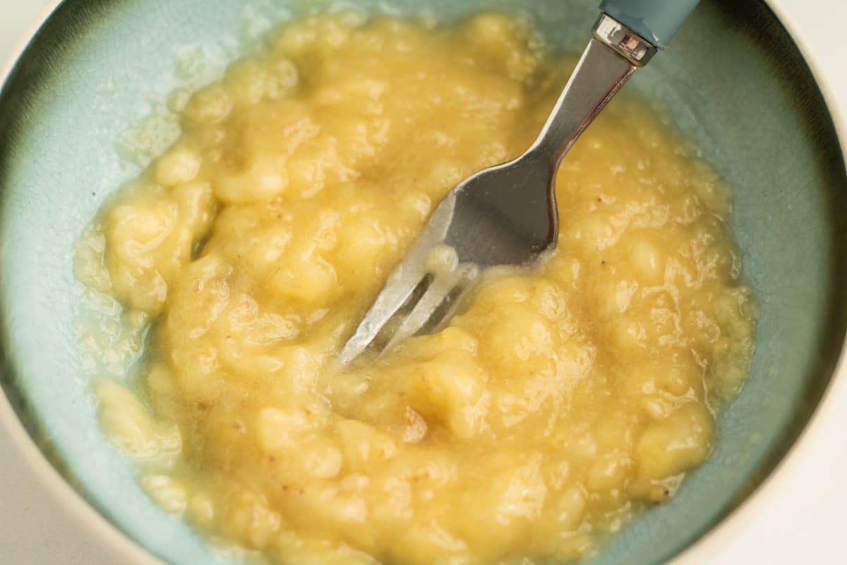 Bananas being mashed in a bowl by a fork.