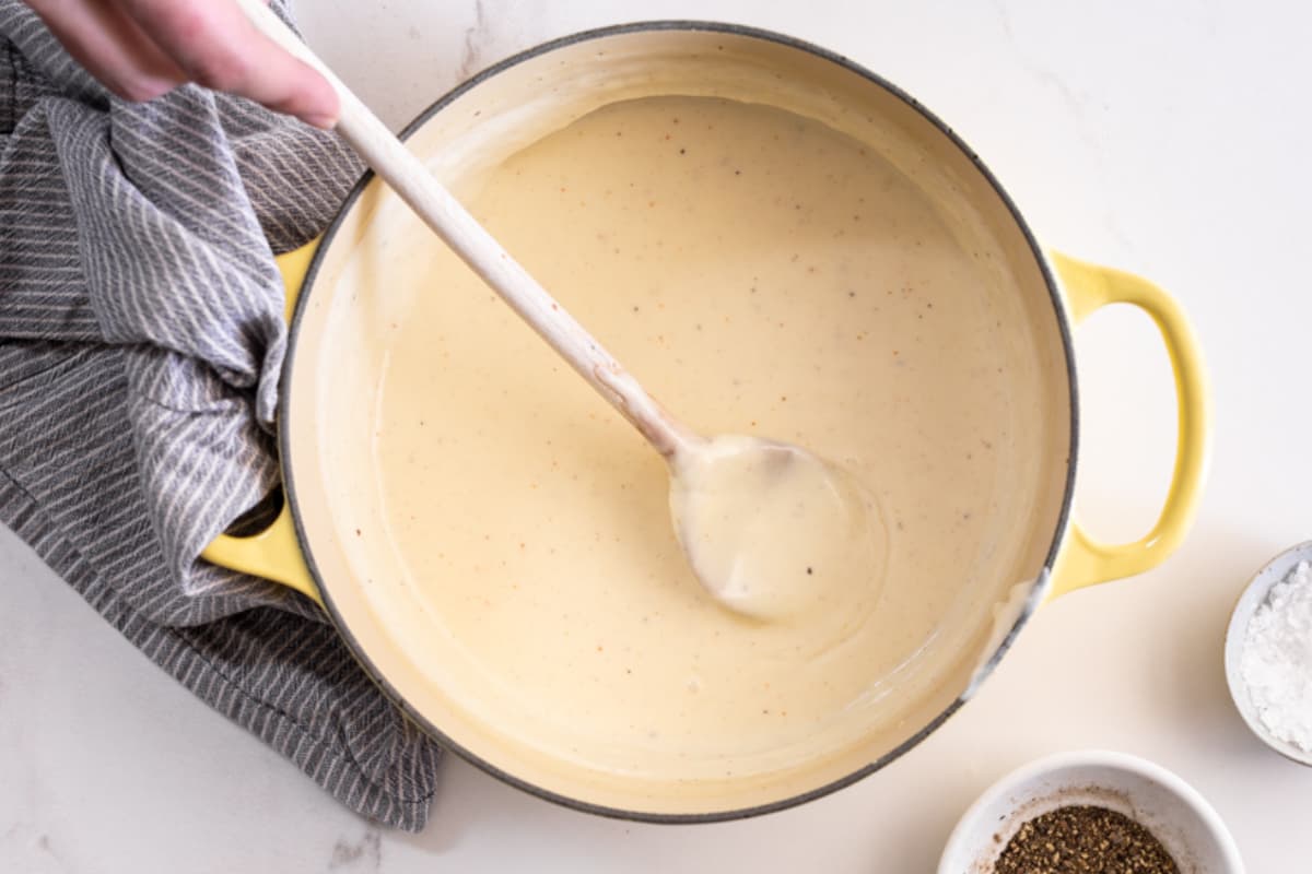 A hand stirring bechamel sauce in a pot.