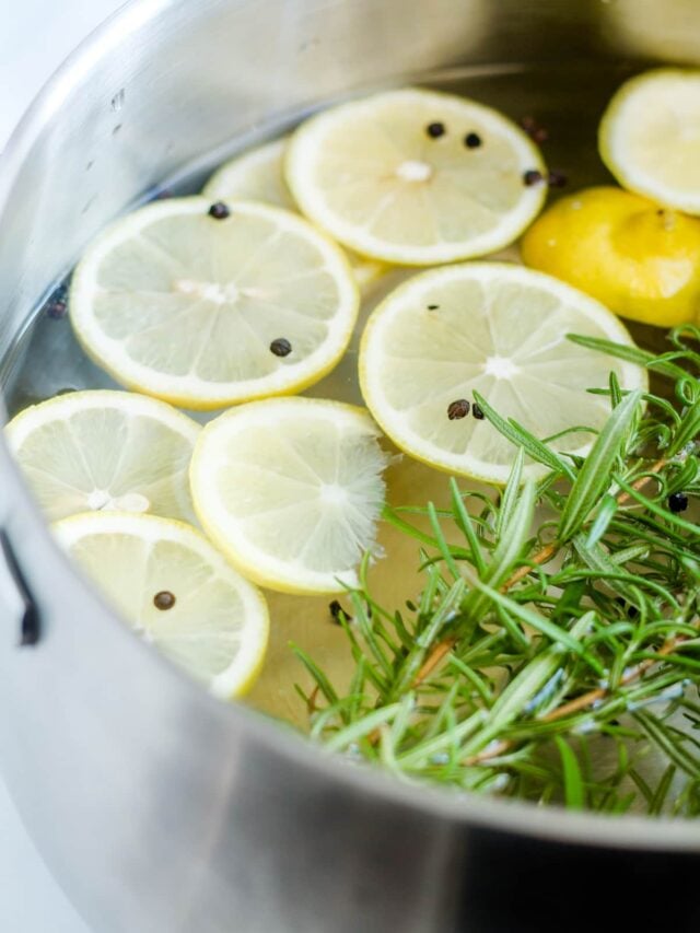 A pot of water with lemons slices and rosemary twigs.