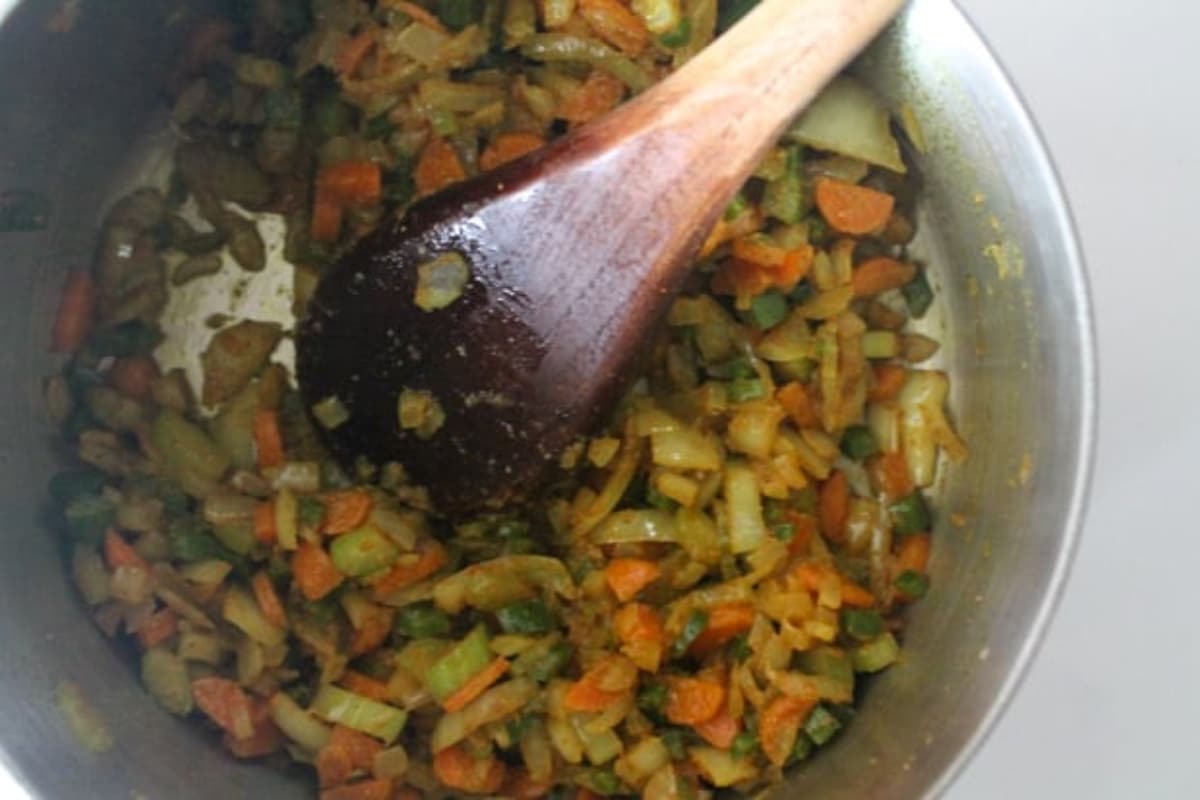 Seasonings being stirred into veggies in a pot.