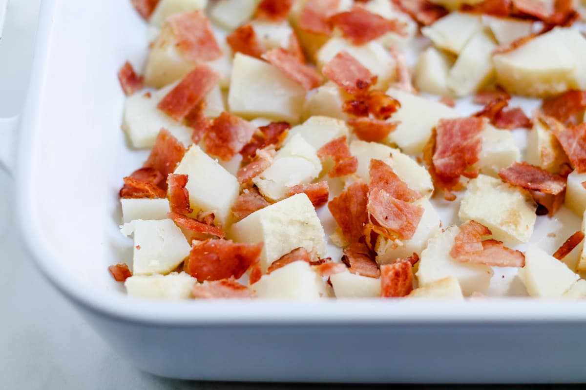 Cooked potatoes and bacon in a casserole dish.