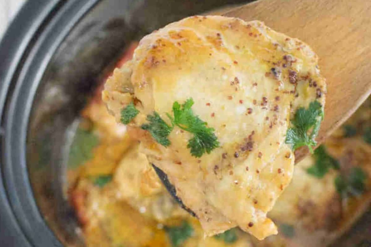 A spoon holding slow cooker honey mustard chicken thighs.