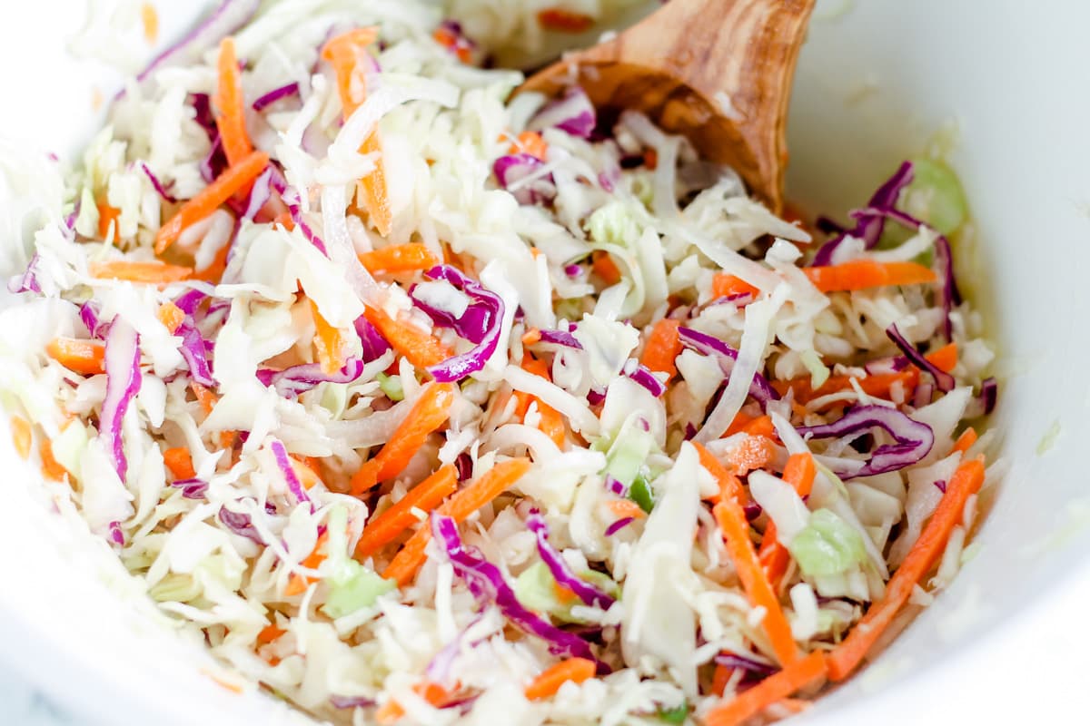 A spoon stirring dressing into the ingredients in a bowl.
