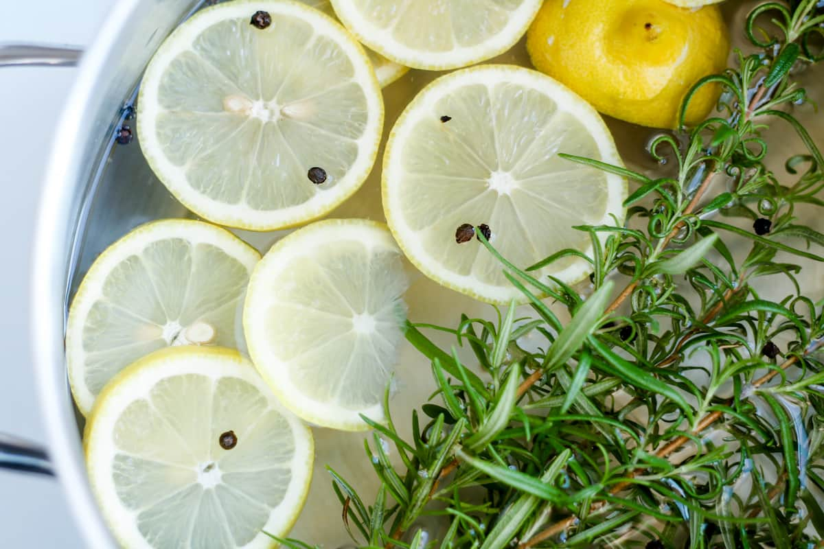 Overhead image of a pot of water with lemons slices and rosemary twigs.