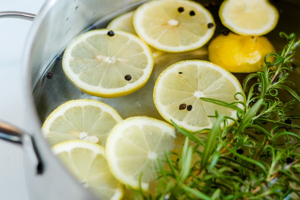 A pot of water with lemons slices and rosemary twigs.