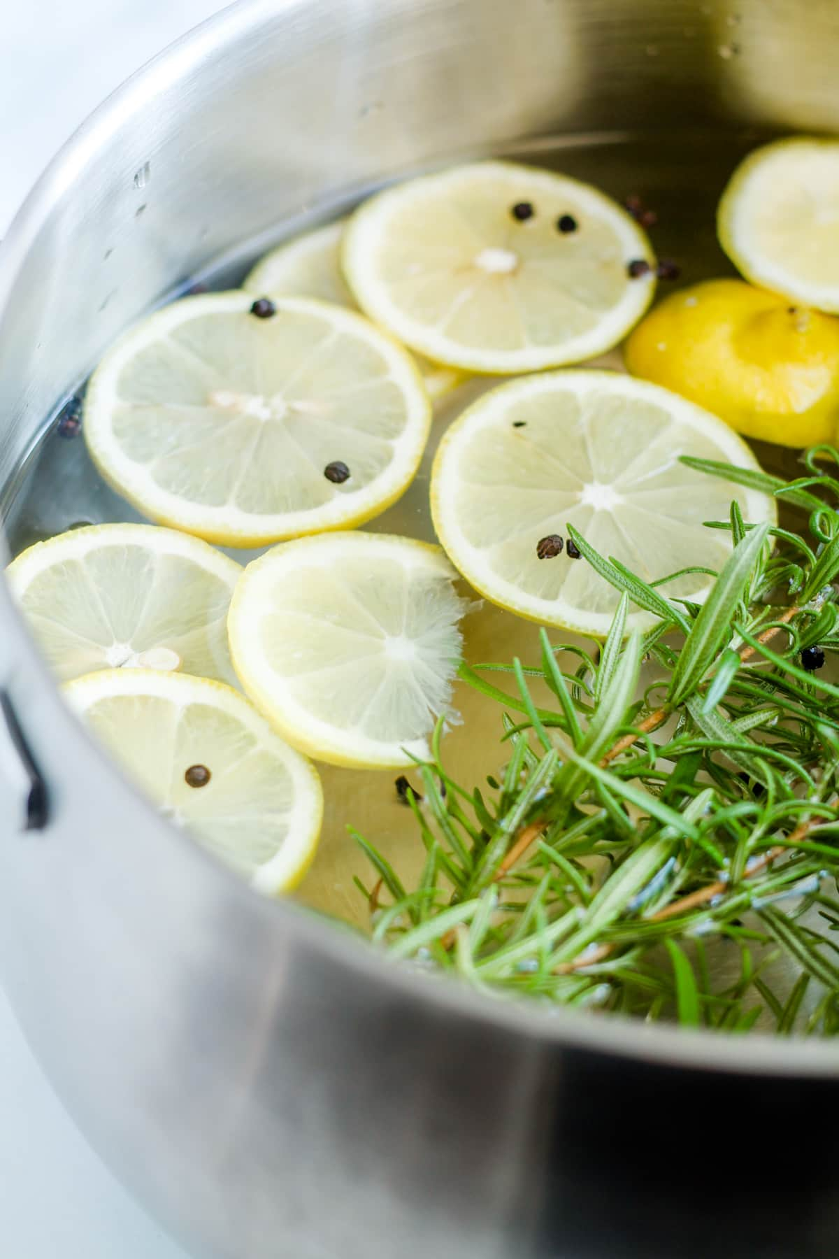 A pot of water with lemons slices and rosemary twigs.