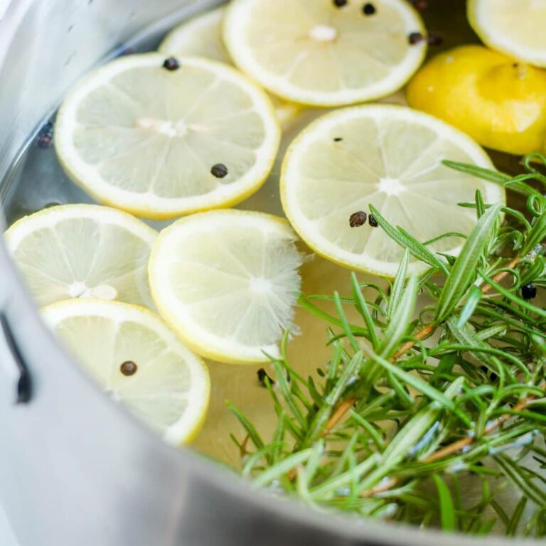 A pot of water with lemons slices and rosemary twigs.