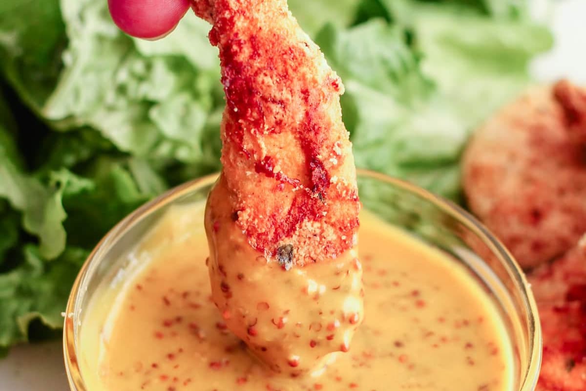 A gluten free chicken tender being dipped into sauce.