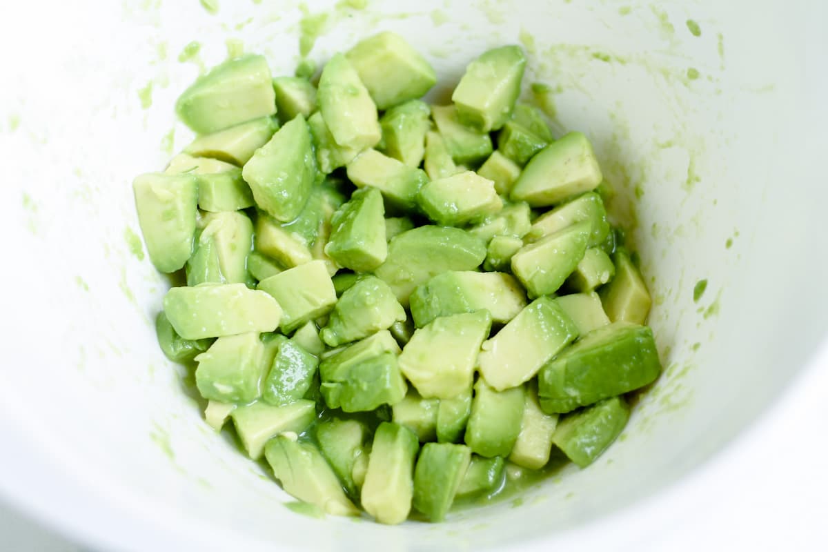 Chopped avocado in a bowl being stirred with lemon juice.