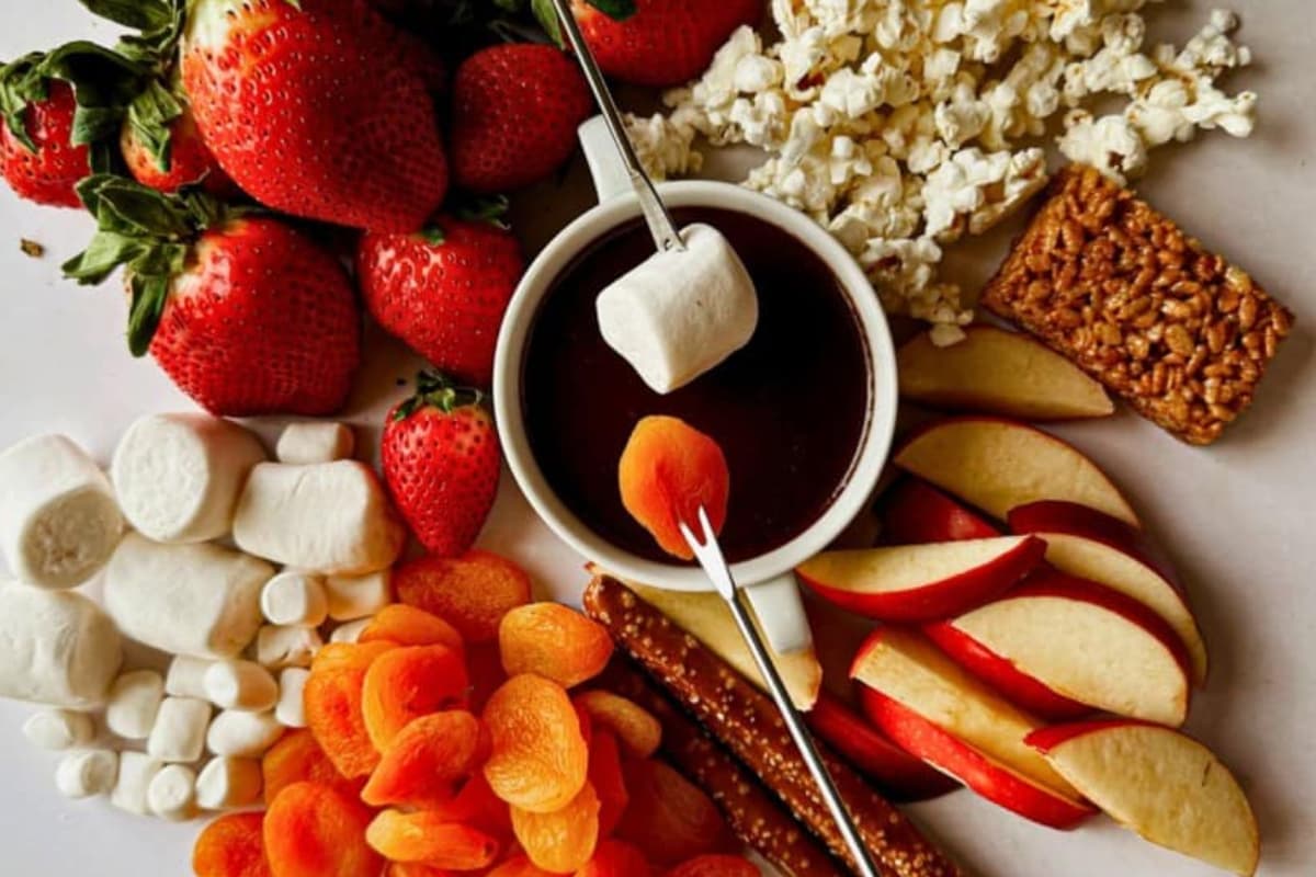 A platter with fruits and a bowl of chocolate hazelnut fondue.