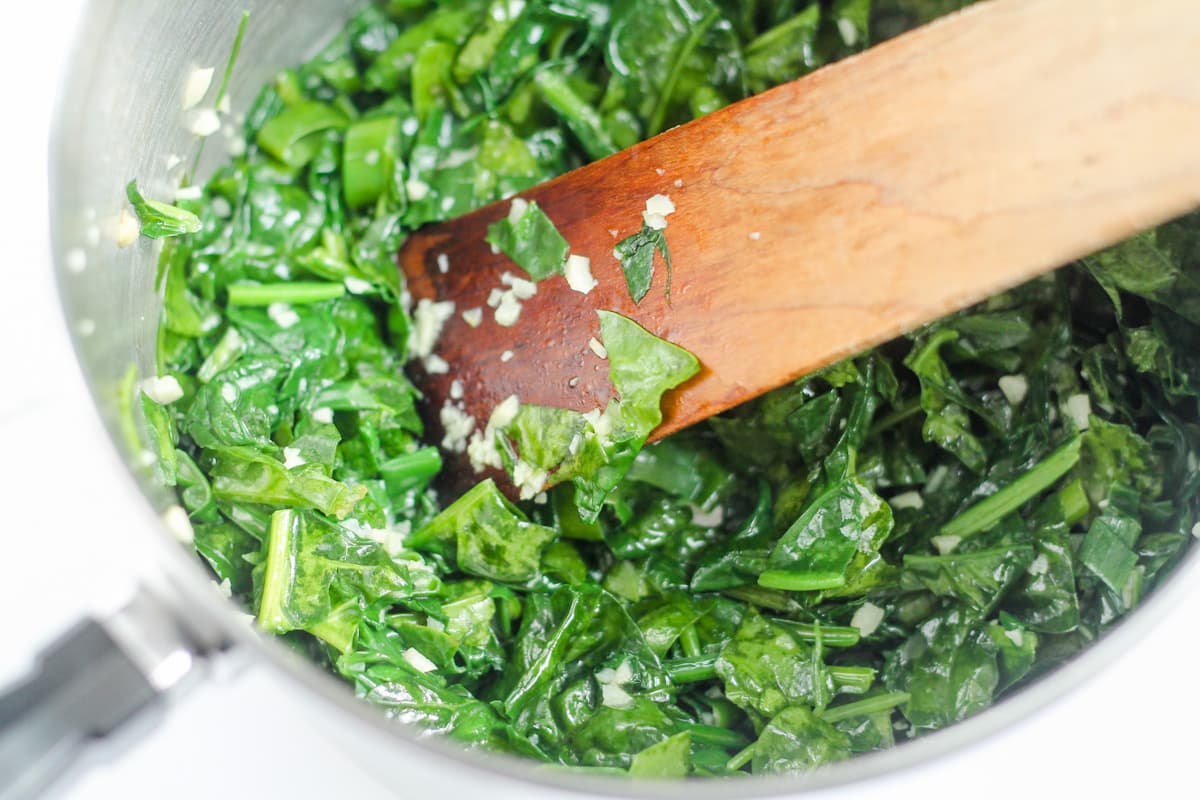 Spinach, onion, and garlic being stirred in a pan.