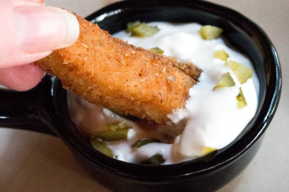 Homemade fish sticks being dipped into sauce.