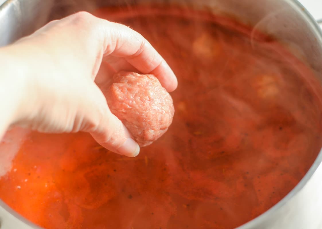 A hand dropping a meatball into a pot.