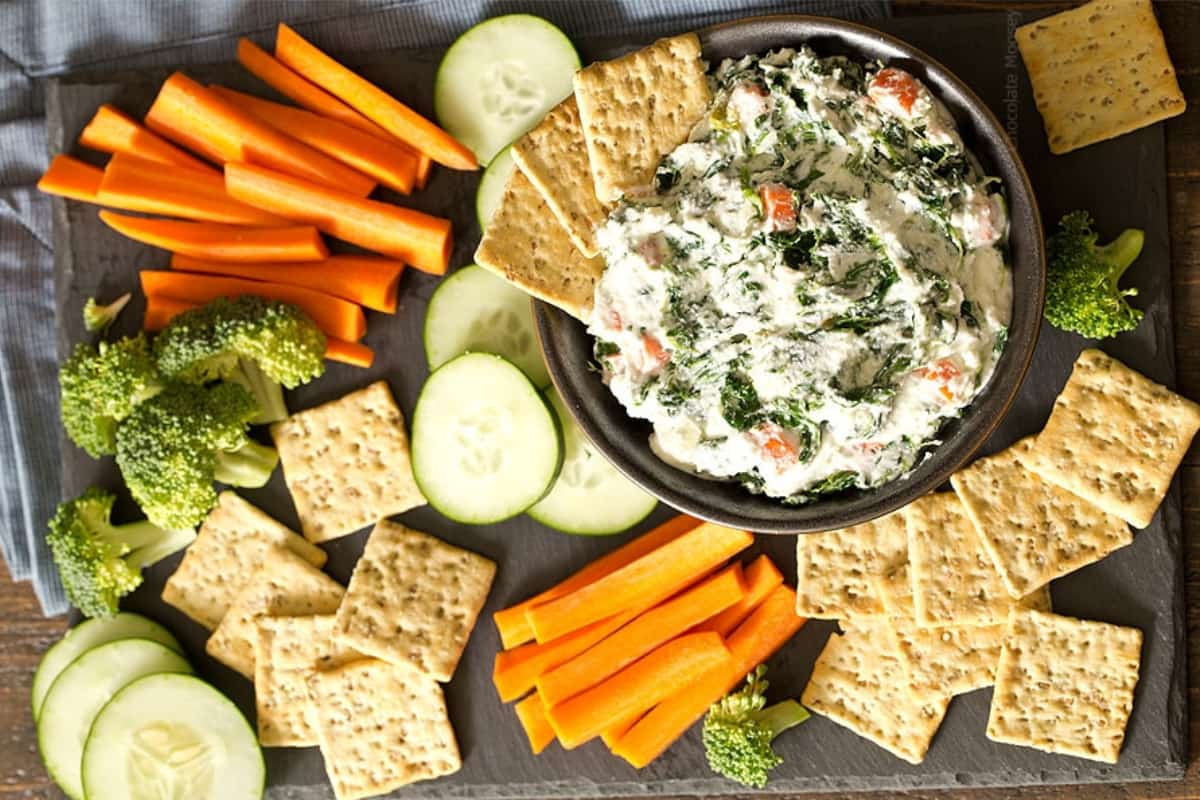 A platter of veggies and crackers with cottage cheese ranch dip.