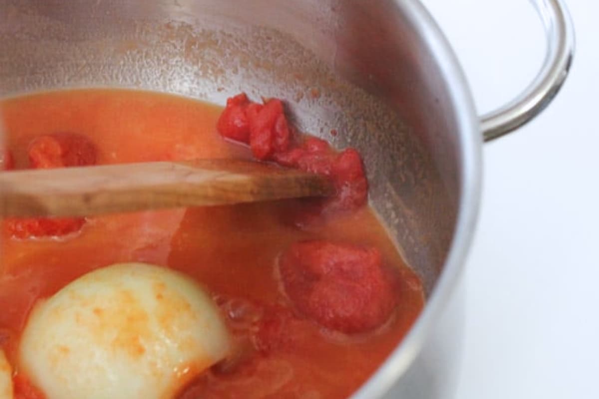 A spoon breaking up tomatoes in a pot.