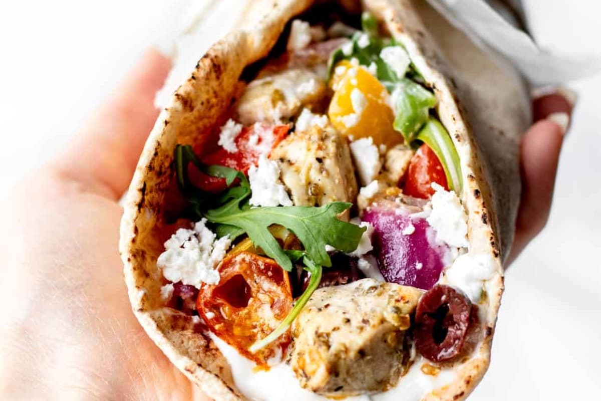 A hand holding sheet pan chicken pitas.