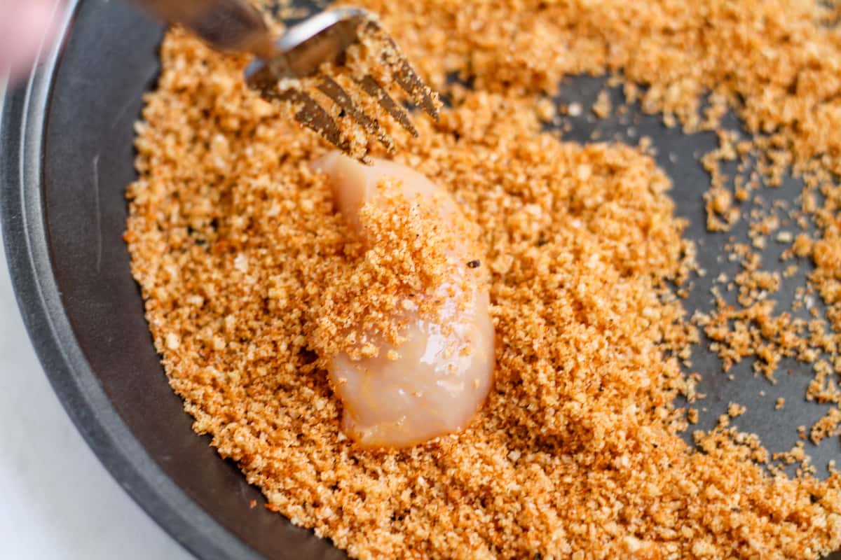 Chicken being coated in pork rinds mixture.