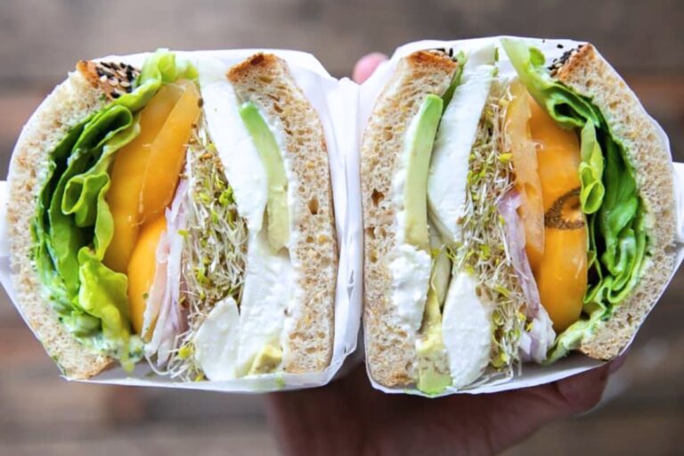 A hand holding a Tomato Mozzarella Sandwich with Herb Mayo.