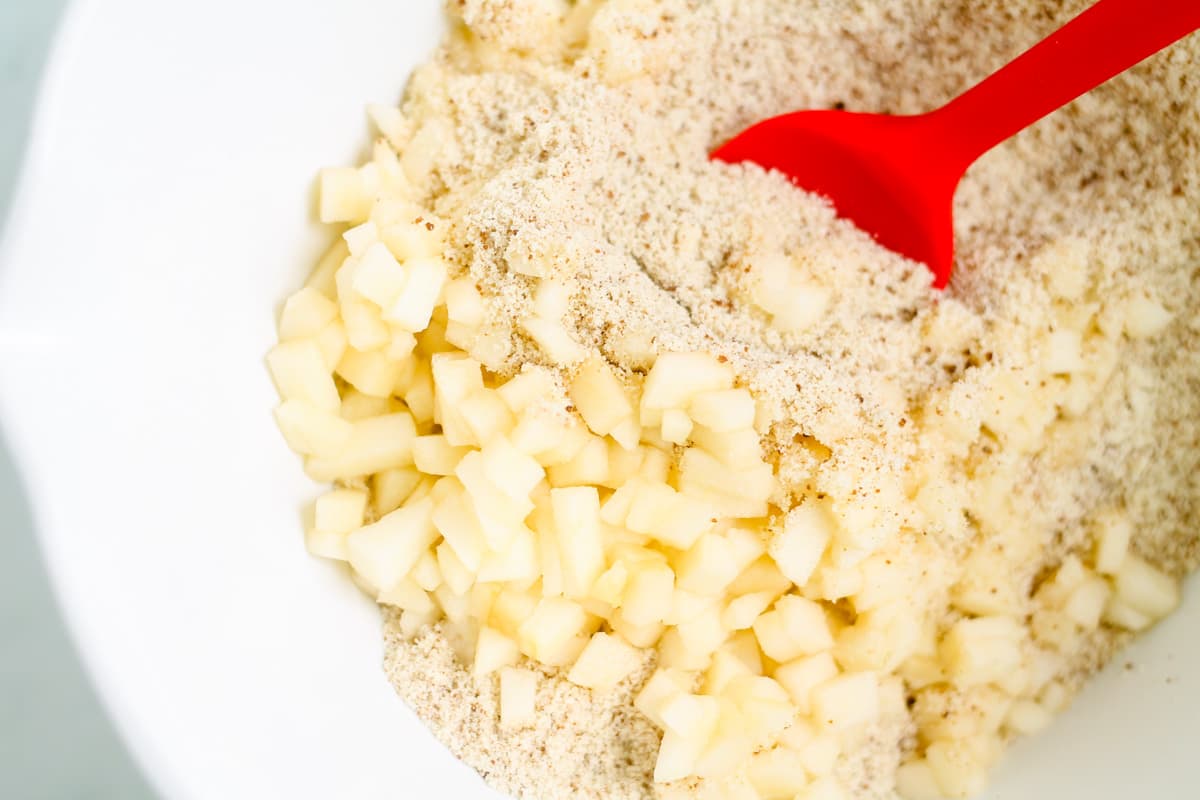 Diced apples being stirred into dry ingredients.