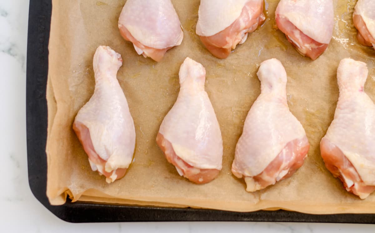 Chicken drumsticks coated in olive oil on a sheet pan.