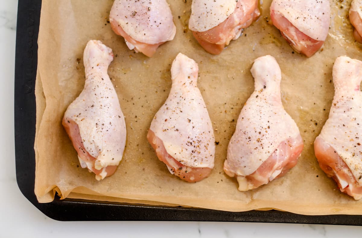 Chicken drumsticks with salt and pepper on a sheet pan.