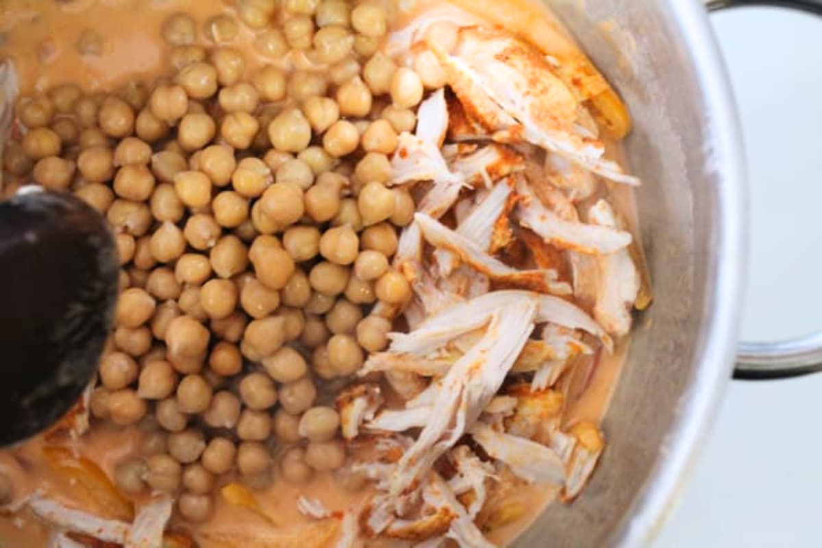 A spoon stirring chickpeas and chicken in a soup pot.