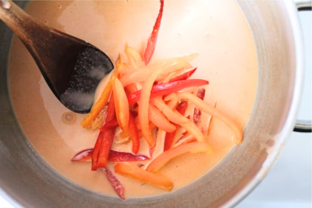 A spoon stirring peppers in a soup pot.