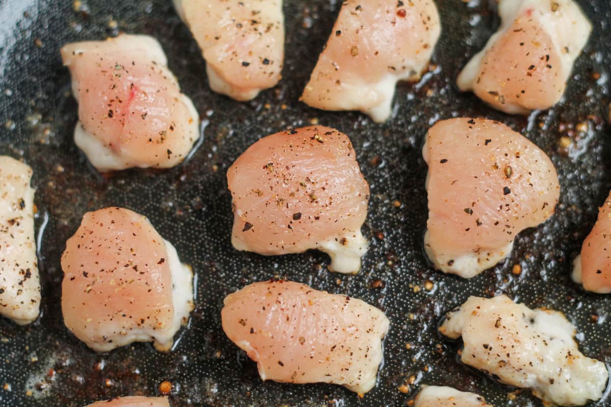 Chicken pieces cooking in a pan.