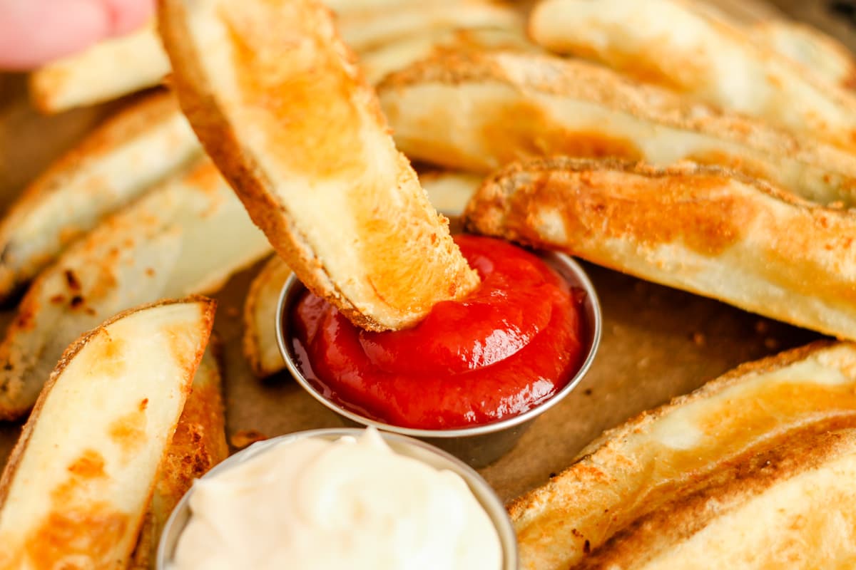 A baked potato wedge being dipped into ketchup.