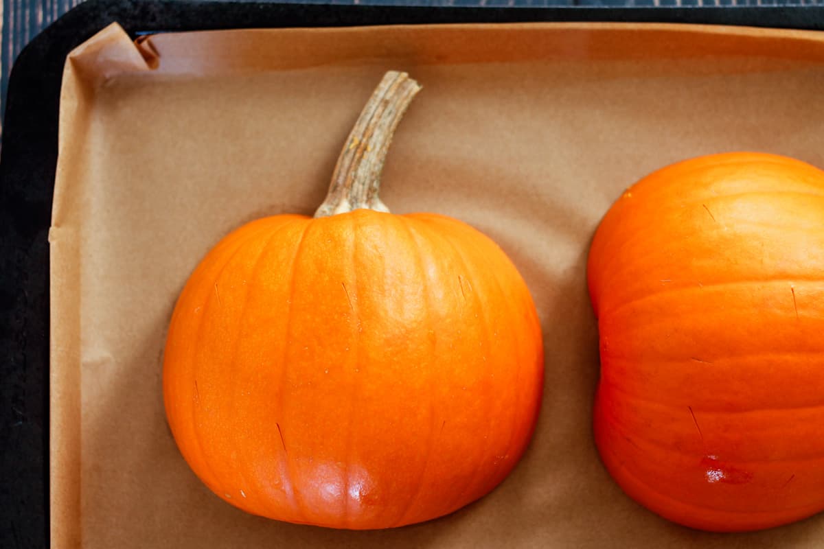 A sheet pan with pumpkin sliced in half face down.