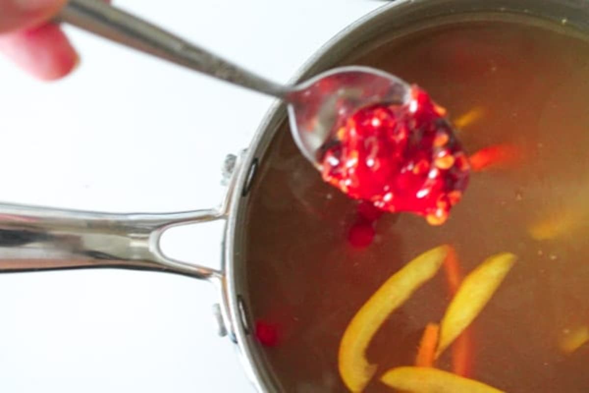 A spoonful of spicy ketchup going into a pot.