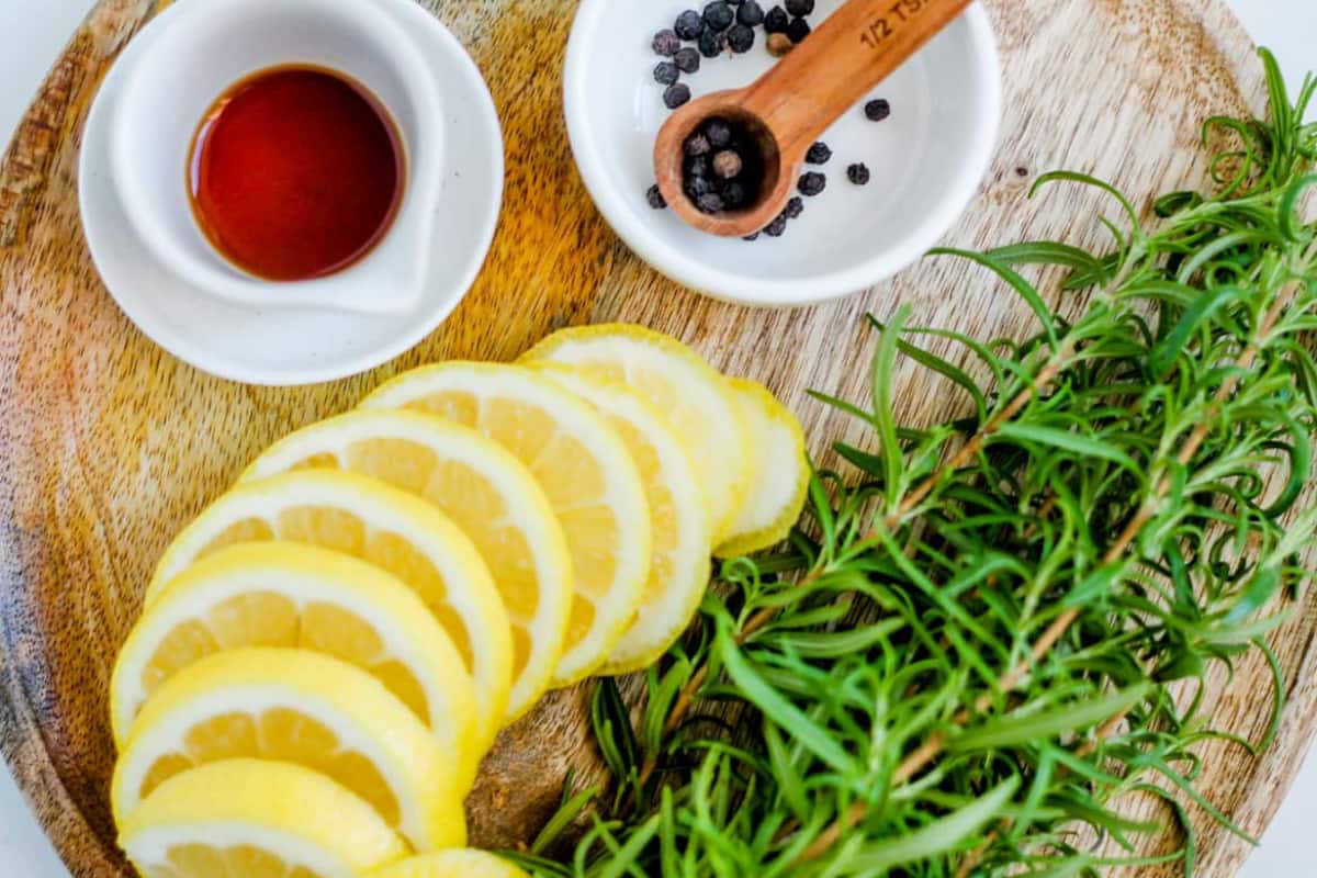 Lemons, fresh rosemary, vanilla extract, and peppercorns on a counter.